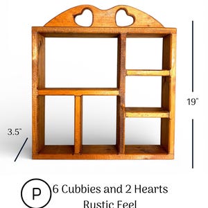 May include: A wooden wall shelf with six cubbies and two heart-shaped cutouts at the top. The shelf measures 16.75 inches wide, 19 inches high, and 3.5 inches deep. The text on the image reads: P 6 Cubbies and 2 Hearts Rustic Feel.