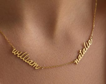 May include: A gold-colored necklace with the names "william" and "natalie" in a cursive font. The necklace is worn against a white collared shirt.