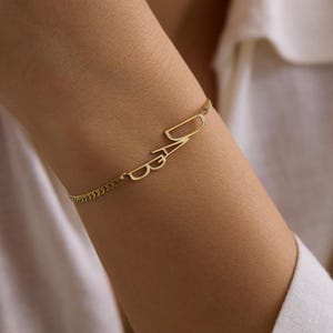 Op de afbeelding: Een goudkleurige armband met het woord "DAD" in een sierlijk, cursief lettertype. De armband heeft een fijne ketting en wordt om de pols gedragen. De letters zijn verbonden en vormen een elegant sieraad.