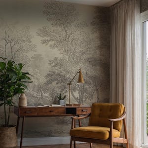 May include: A home office setup featuring a wooden desk with drawers, a mustard-colored armchair, and a potted plant. The wall is adorned with a black and white forest-themed wallpaper, and a gold desk lamp sits on the desk.