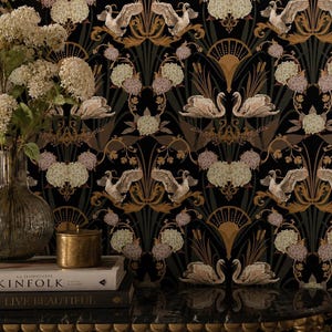 May include: Wallpaper featuring a repeating pattern of white swans, gold art deco fan motifs, and clusters of pale flowers against a black background. A clear ribbed glass vase with white hydrangea flowers sits in front of the wallpaper.