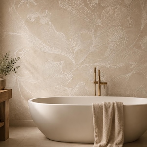 May include: A white oval freestanding bathtub with a beige towel draped over the side, positioned in front of a textured beige wall with white floral patterns. A wooden vanity with a stone sink and brass faucet sits to the left of the tub.