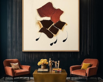May include: An abstract painting with a cream background and a gold frame. The artwork features shapes in shades of brown and red, with black teardrop-like accents. Two orange armchairs flank a gold coffee table with decor.