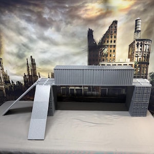 May include: A gray miniature shipping container structure featuring a long elevated bridge section supported by two vertical container towers, with a flat ramp extending from the left side, all constructed with a textured, corrugated surface.