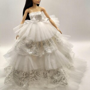May include: A white bridal gown with a strapless bodice and a full skirt made of layers of tulle and lace.