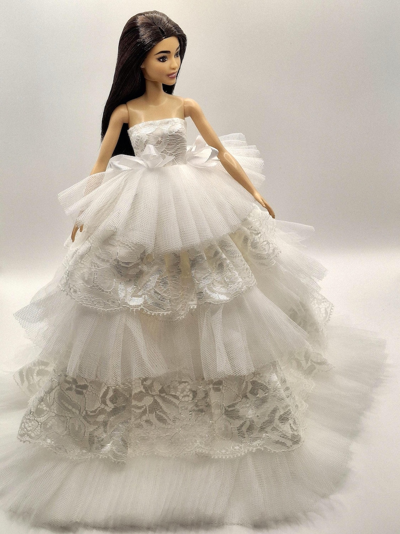 May include: A white bridal gown with a strapless bodice and a full skirt made of layers of tulle and lace.