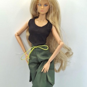 May include: A fashion doll with long blonde hair, wearing a black sleeveless top and olive green cargo pants with large side pockets. The pants feature a bright neon yellow drawstring at the waist. The doll has articulated limbs.