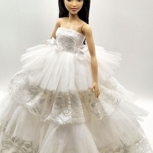 May include: A white strapless doll dress with a lace bodice and tulle skirt. The dress has multiple layers of tulle and lace, creating a voluminous and elegant look.