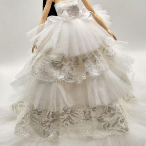 May include: A white strapless tulle wedding dress with lace trim and a large bow at the waist.