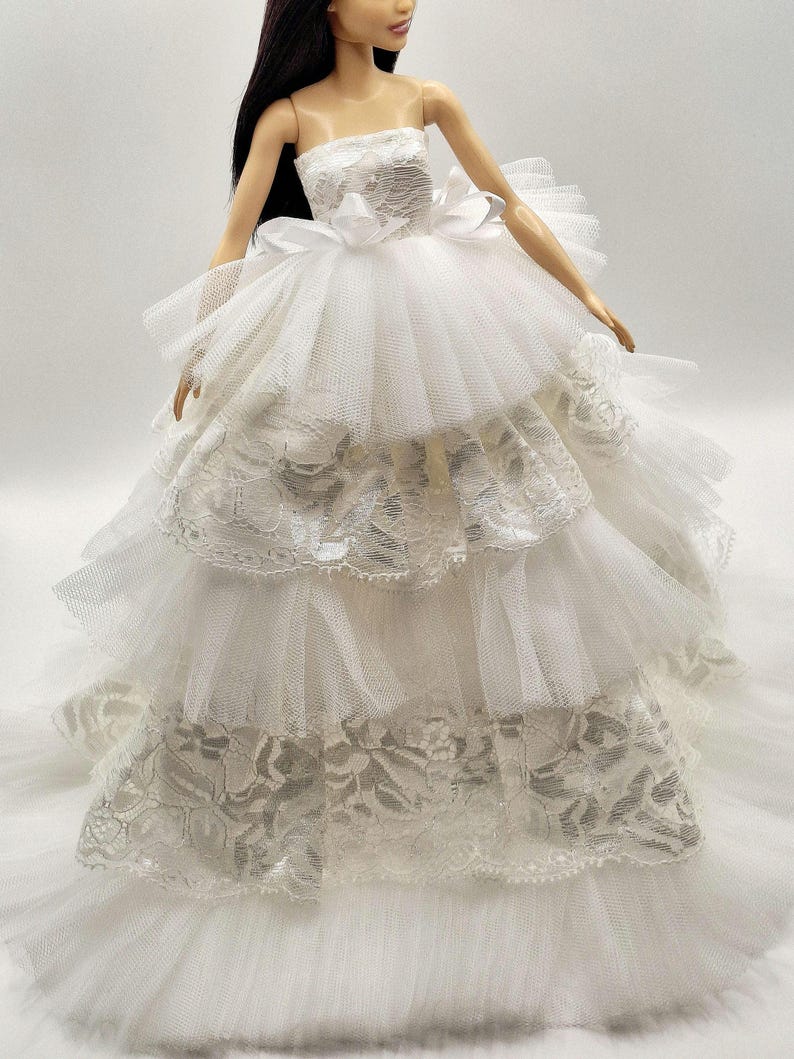 May include: A white strapless tulle wedding dress with lace trim and a large bow at the waist.