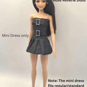 K&ouml;nnte beinhalten: Eine Puppe mit langem dunklem Haar tr&auml;gt ein schwarzes, tr&auml;gerloses Minikleid mit zwei silberfarbenen Schnallen. Der Text lautet: Rose Reverie Dolls, Mini Dress only, Note: The mini dress fits regular/standard and petite doll only.