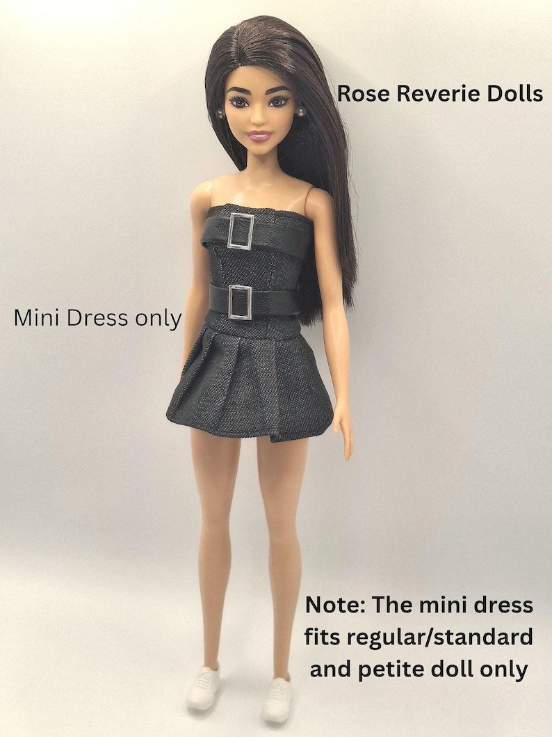 K&ouml;nnte beinhalten: Eine Puppe mit langem dunklem Haar tr&auml;gt ein schwarzes, tr&auml;gerloses Minikleid mit zwei silberfarbenen Schnallen. Der Text lautet: Rose Reverie Dolls, Mini Dress only, Note: The mini dress fits regular/standard and petite doll only.