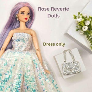 K&ouml;nnte beinhalten: Eine Puppe in einem tr&auml;gerlosen wei&szlig;en Kleid mit blauen und t&uuml;rkisfarbenen Pailletten. Die Puppe hat langes lavendelfarbenes Haar und tr&auml;gt Ohrringe. Eine kleine, glitzernde Handtasche und eine Vase mit wei&szlig;en Blumen sind ebenfalls im Bild. Der Text lautet "Rose Reverie Dolls" und "Dress only."