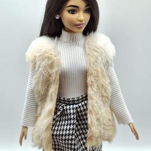 May include: A fashion doll wearing a white turtleneck sweater, a faux fur vest in shades of beige and cream, and a black and white houndstooth skirt. The doll has dark hair and is wearing pearl earrings.