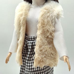 May include: A doll wearing a cream-colored faux fur vest over a white turtleneck sweater. The doll is also wearing a black and white houndstooth skirt. The doll is wearing a pearl earring.