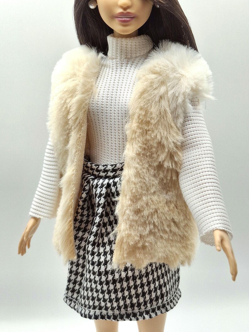 May include: A doll wearing a cream-colored faux fur vest over a white turtleneck sweater. The doll is also wearing a black and white houndstooth skirt. The doll is wearing a pearl earring.