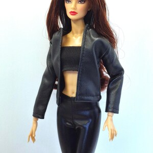 May include: A fashion doll with long auburn hair, wearing a black faux leather jacket, a black tube top, and black pants. The doll has red lipstick and is posed against a white background. The jacket is open, revealing the top and midriff.