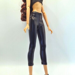 May include: A doll wearing a black tube top, black capri pants, and black ankle boots. The doll has long, wavy auburn hair. The outfit is a sleek, modern style.