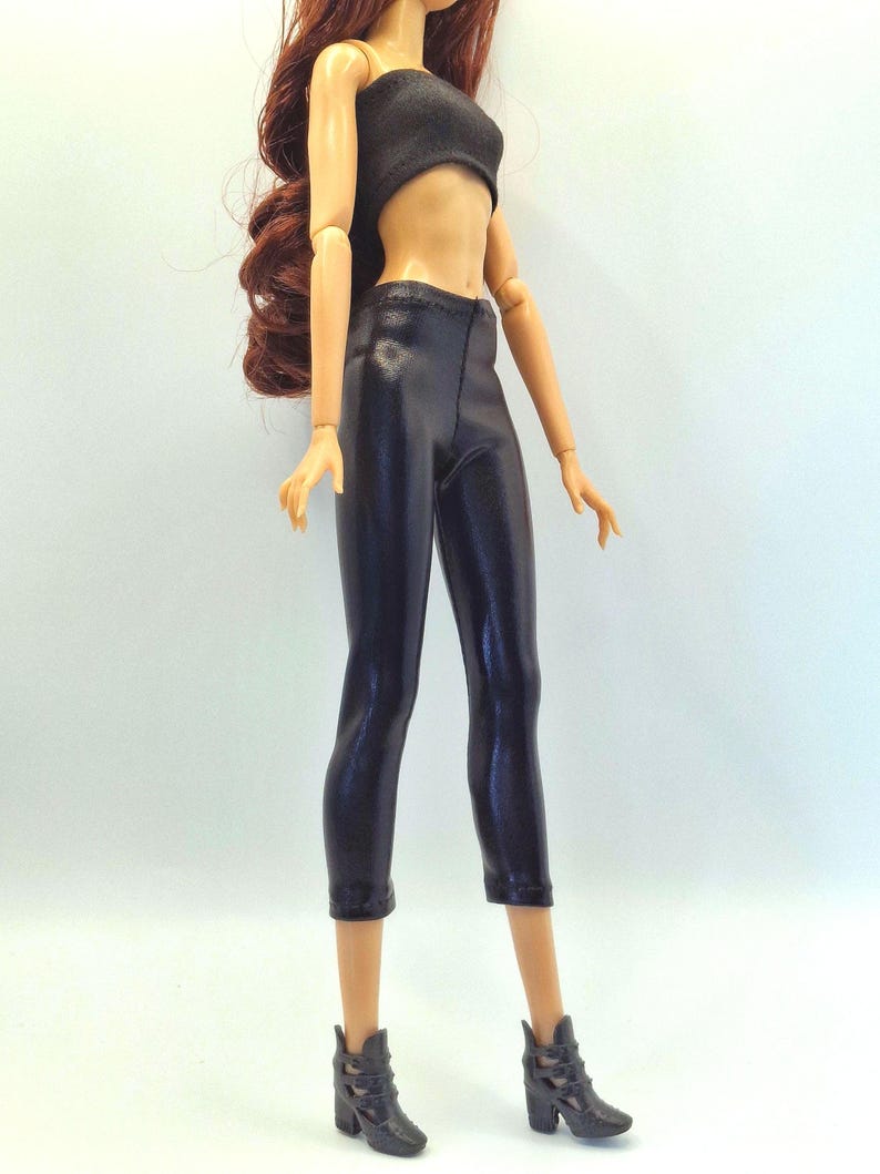 May include: A doll wearing a black tube top, black capri pants, and black ankle boots. The doll has long, wavy auburn hair. The outfit is a sleek, modern style.