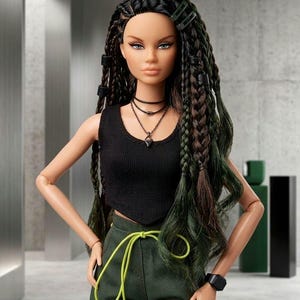 May include: A fashion doll with long dark hair styled in braids and loose waves, wearing a black sleeveless crop top, dark green cargo pants with a bright lime green drawstring, a layered necklace, and a black wristwatch on the left wrist.