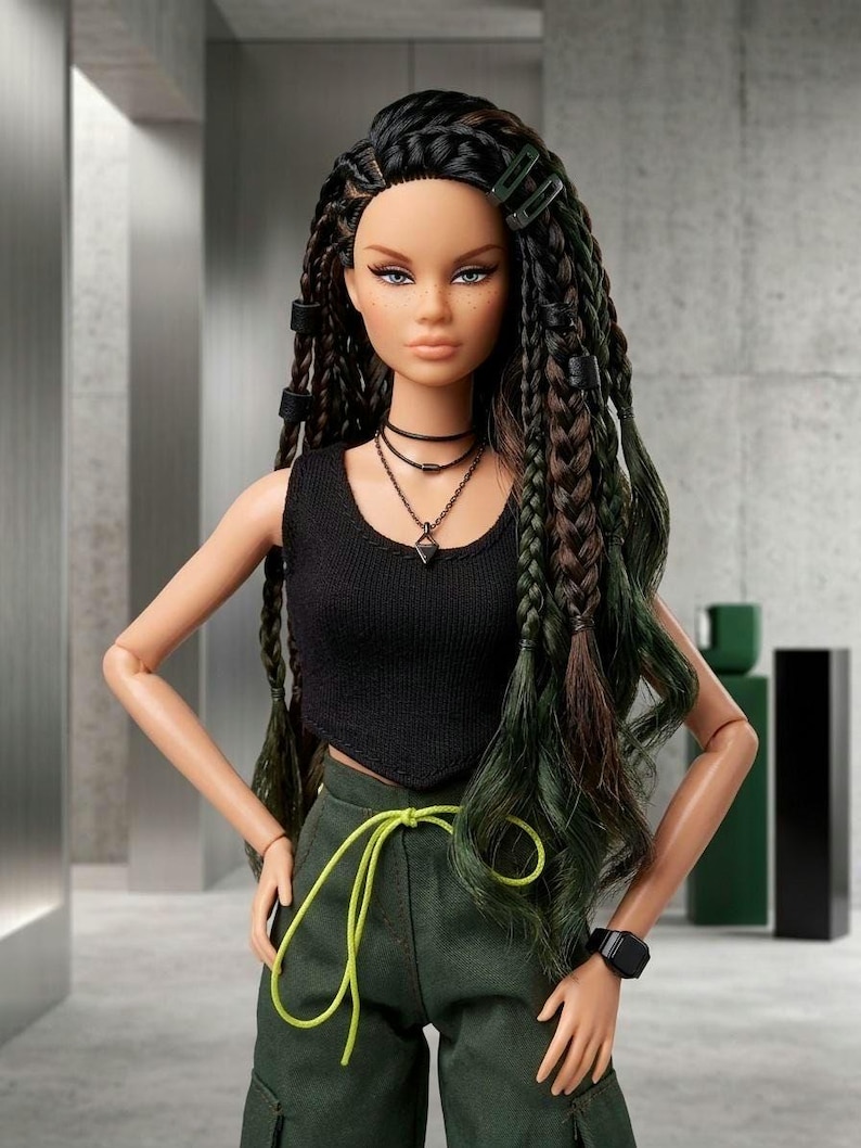May include: A fashion doll with long dark hair styled in braids and loose waves, wearing a black sleeveless crop top, dark green cargo pants with a bright lime green drawstring, a layered necklace, and a black wristwatch on the left wrist.