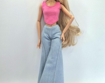 May include: A fashion doll with long blonde hair wearing a sleeveless pink cropped top with a rounded neckline and light blue denim-style flared trousers. The doll has articulated limbs and is standing in a neutral pose against a plain background.