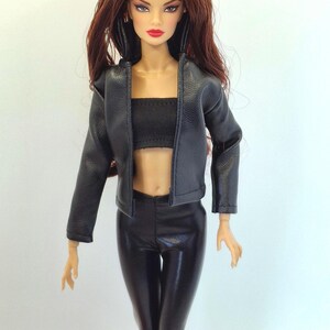 May include: A fashion doll with long auburn hair, wearing a black leather jacket, a black tube top, and black shiny pants. The doll has red lipstick and is posed against a white background.