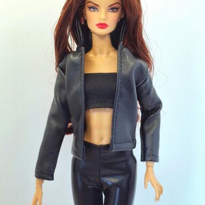 May include: A fashion doll with long auburn hair, wearing a black leather jacket, a black tube top, and black shiny pants. The doll has red lipstick and is posed against a plain background. The doll's outfit is a modern style.
