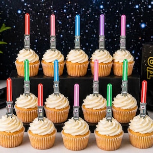 Könnte beinhalten: Ein Dutzend Cupcakes mit weißem Zuckerguss, jeweils mit einem farbenfrohen Lichtschwert-förmigen Pick verziert. Die Lichtschwerter sind rot, rosa, blau, grün und lila. Die Cupcakes sind auf einem schwarzen, mehrstöckigen Ständer angeordnet.