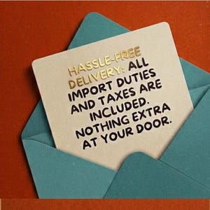 May include: A square card with gold lettering is inside a teal envelope. The card reads "HASSLE-FREE DELIVERY: ALL IMPORT DUTIES AND TAXES ARE INCLUDED. NOTHING EXTRA AT YOUR DOOR."