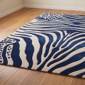 May include: A rectangular rug with a striking zebra stripe pattern in navy blue and off-white. The rug also features leopard print accents on the corners. The rug is placed on a hardwood floor.