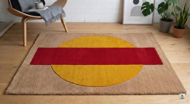 May include: A rectangular area rug with a geometric design. The rug features a large yellow circle with a red rectangular stripe across the center. The rug has a tan border and is placed on a wooden floor.