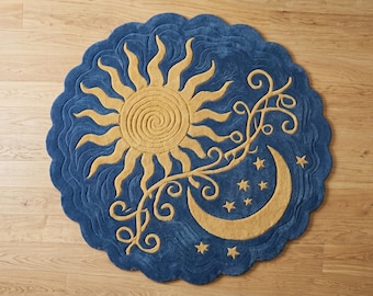 May include: A round, blue rug with a celestial design. The rug features a golden sun, crescent moon, stars, and decorative vines. The rug has a scalloped edge and is placed on a wooden floor.