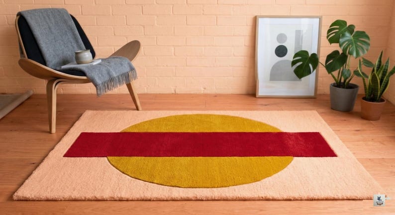 May include: A rectangular rug with a peach-colored background, featuring a large yellow circle and a red rectangular stripe across the center. The rug is placed on a wooden floor, with a chair and artwork in the background.