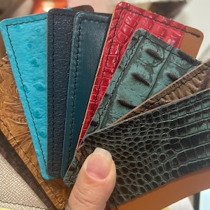 May include: A selection of leather swatches in diverse colours and textures. The samples feature embossed, ostrich, and crocodile patterns in shades of brown, turquoise, navy, teal, red, and black. Each swatch is rectangular with a stitched edge.