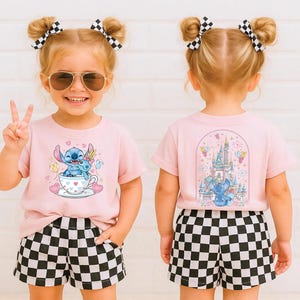 Puede incluir: Un conjunto infantil con una camiseta rosa con un dise&ntilde;o de dibujos animados de Stitch y pantalones cortos a cuadros blancos y negros. La parte delantera de la camiseta muestra a Stitch en una taza de t&eacute;, mientras que la parte trasera muestra una escena de castillo. El ni&ntilde;o tambi&eacute;n lleva gafas de sol y lazos para el pelo.