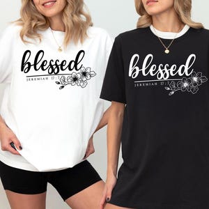 May include: Two t-shirts, one white and one black, featuring the word "blessed" in cursive with floral details. The text "Jeremiah 17:7" is printed below. The shirts are casual wear.