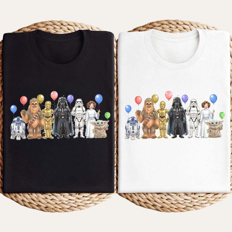 May include: Two t-shirts, one black and one white, each featuring a colorful illustration of Star Wars characters holding balloons. The characters include R2-D2, Chewbacca, C-3PO, Darth Vader, a Stormtrooper, Princess Leia, and Grogu.