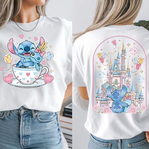 Puede incluir: Camiseta blanca con un dise&ntilde;o de dibujos animados de Stitch. La parte delantera muestra a Stitch en una taza de t&eacute; con corazones y globos. La parte trasera presenta un castillo con Stitch y globos. El dise&ntilde;o utiliza colores rosa, azul y amarillo.