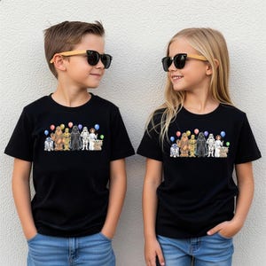 May include: Two children wearing black t-shirts featuring a Star Wars character design with balloons. The design includes characters like R2-D2, Chewbacca, Darth Vader, and others. The children are also wearing sunglasses.