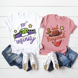 May include: Two t-shirts, one white and one pink, with the phrases "To Infinity" and "And Beyond". The white shirt has a green and purple spaceship design. The pink shirt features a cowboy hat and boot graphic. Both shirts are paired with blue jeans and white trainers.