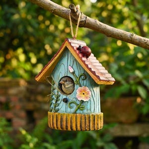 Könnte beinhalten: Ein dekoratives Vogelhaus in Blau-, Gelb- und Brauntönen, mit einem kleinen Vogel, der aus der Öffnung schaut. Auf dem Dach sitzt ein roter Marienkäfer. Das Vogelhaus hängt an einem Ast.