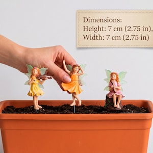 May include: Three fairy figurines with translucent wings, each wearing a floral crown and a dress in yellow, orange, or pink. The figurines are mounted on stakes and measure 2.75 inches in height and 2.75 inches in width, as shown in the text.