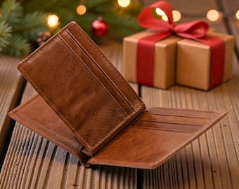 May include: Open brown leather wallet with card slots, displayed on a wooden surface. A wrapped gift box with a red ribbon and Christmas tree with lights are in the background. The wallet is a bi-fold style.