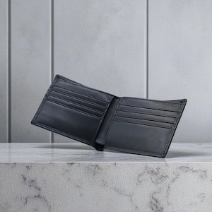 May include: Open black leather wallet with several card slots and bill compartments. The wallet is shown open, displaying its interior design. The background is a neutral grey, highlighting the wallet's features.