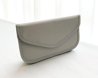 May include: A light gray, rectangular glasses case with a curved flap closure. The case is made of a textured fabric and features a stitched border. The design is simple and minimalist, suitable for protecting eyewear.