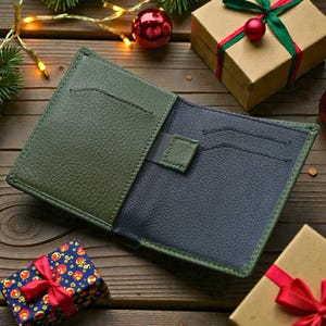 May include: Open olive green and navy blue leather wallet with card slots. The wallet is on a wooden surface, surrounded by wrapped gifts and Christmas decorations.