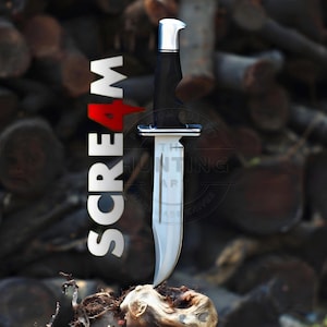 May include: A fixed-blade knife with a silver-colored steel blade, a black handle, and a silver pommel. The word SCREAM is printed vertically in white and red letters to the left of the knife, which is positioned upright on a textured base.
