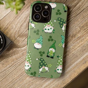 May include: Green phone case featuring a pattern of St. Patrick's Day gnomes and shamrocks. The gnomes wear green hats with various patterns, and the case has a glossy finish. The case is designed for a smartphone with multiple camera lenses.