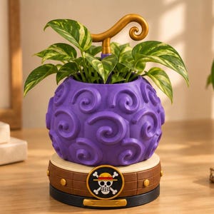 May include: A purple, spherical planter with a textured swirl pattern and a gold-colored stem handle. The planter sits on a brown, circular base featuring a black and white skull and crossbones emblem with a red and yellow hat on top of the skull.